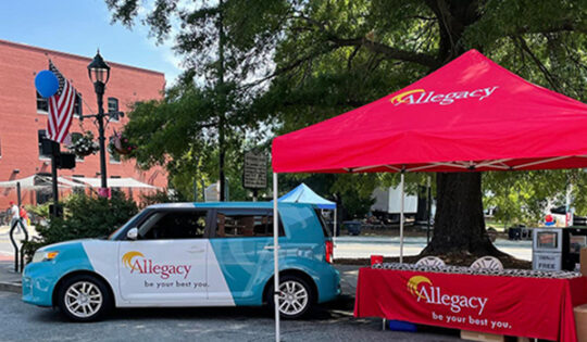 The Allegacy car and a bright red Allegacy tent setup in downtown Greensboro for the Fun Fourth event