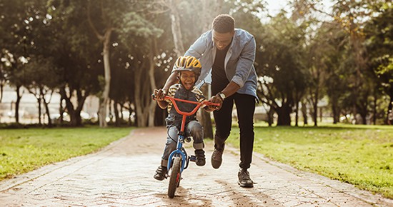 Boy learning to ride a bicycle with his father in park.