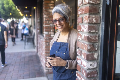 mature business woman with glasses standing in doorway of brick shop front with a warm smile