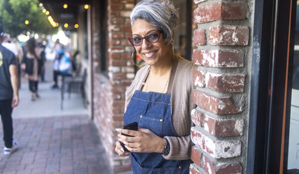 mature business woman with glasses standing in doorway of brick shop front with a warm smile