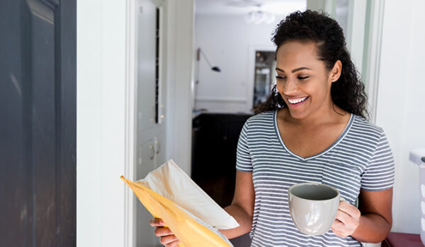 mid adult woman carrying a cup of coffee in sunny hallway smiling while looking at mail