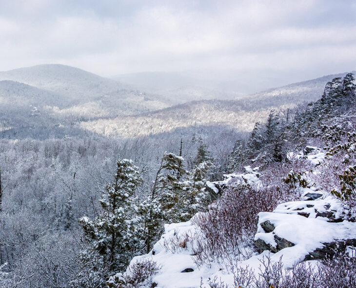 wide landscape view of Blue Ridge Mountains covered in snow with mottled clouds and sun