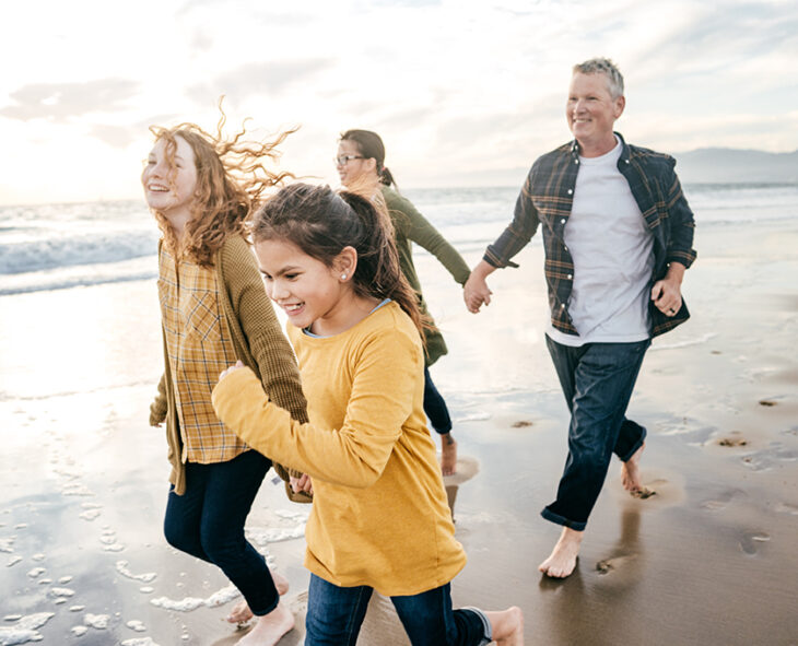 happy smiling family with tween and teenage daughters walking in front of their parents on beach