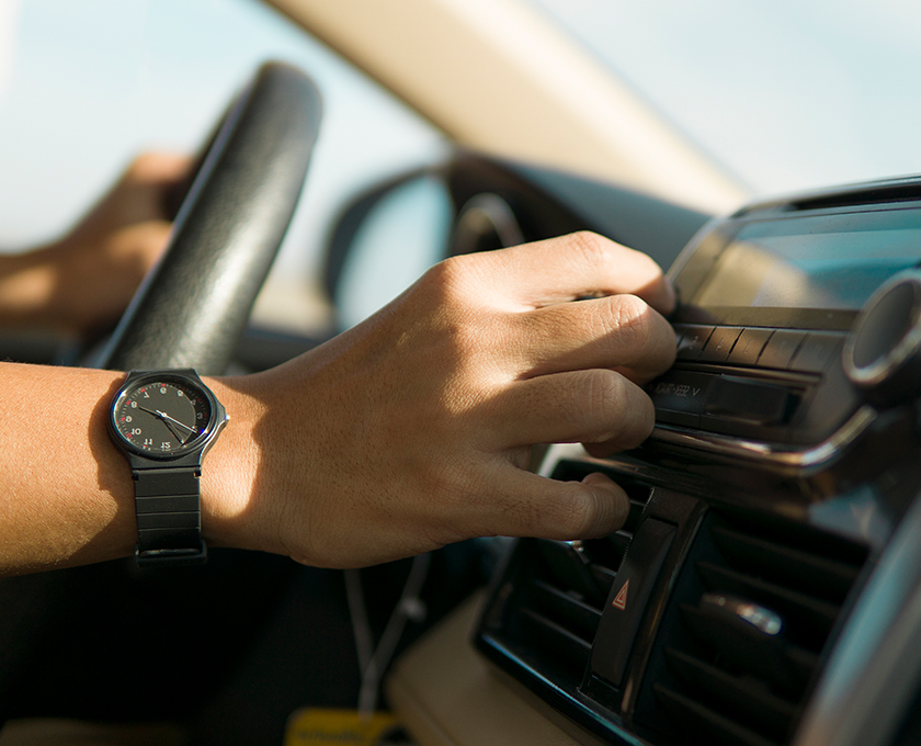 close up of a hand reaching for temperature control knob in car while other hand remains on steering wheel