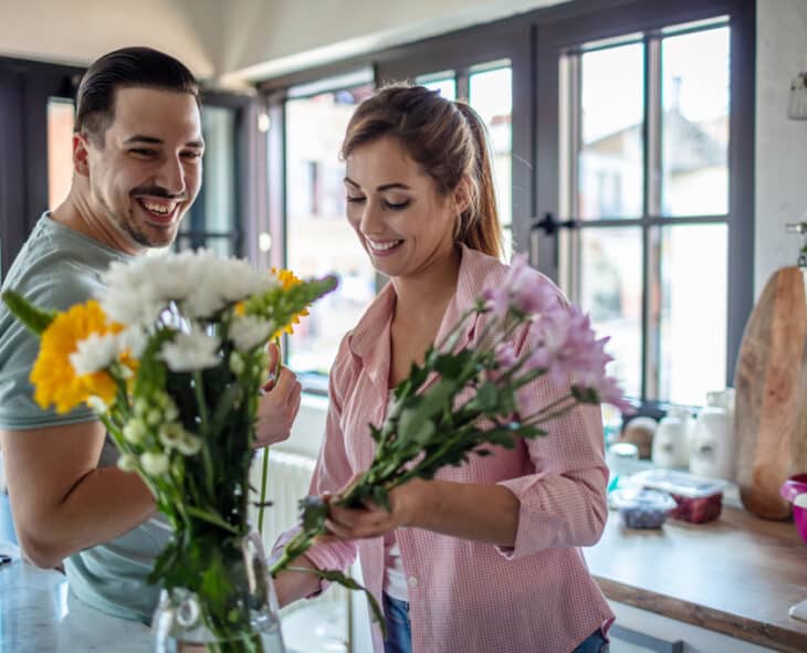 Young couple in home kitchen arranging wildflowers in a vase