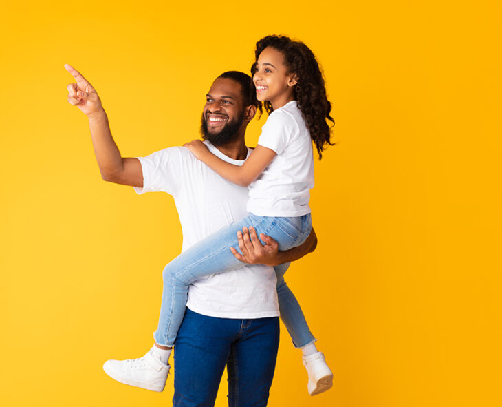 cheerful dad holding excited tween daughter up high and pointing
