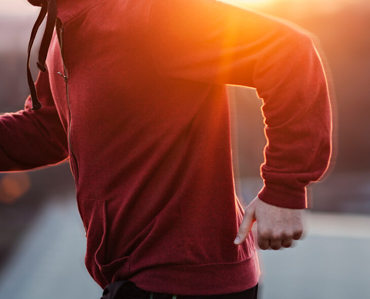 close up of man running in red zip up hoodie with warm sunlight behind him