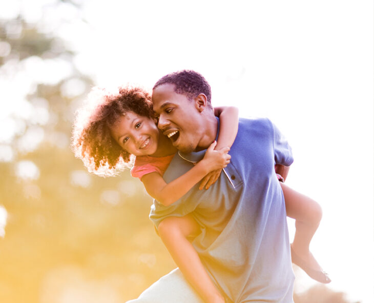 Playful father piggybacking his daughter outdoors having fun in nature