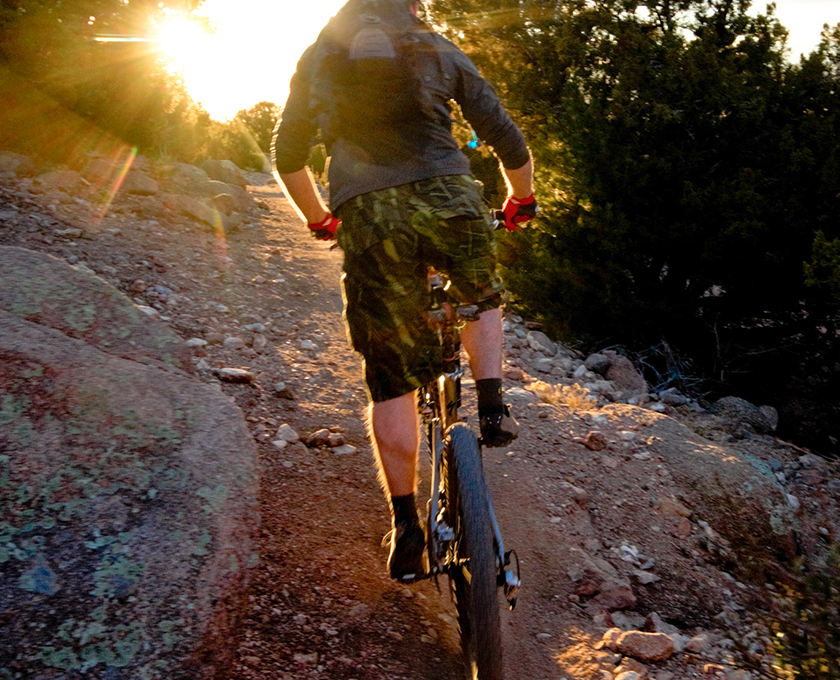 man in outdoor gear riding a mountain bike on rough trail with sun shining brightly