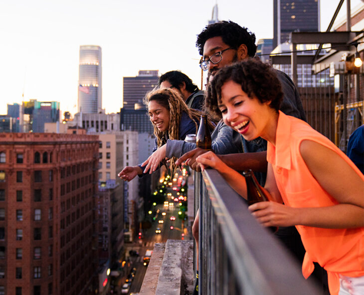 group of friends looking over rooftop apartment railing at downtown streets