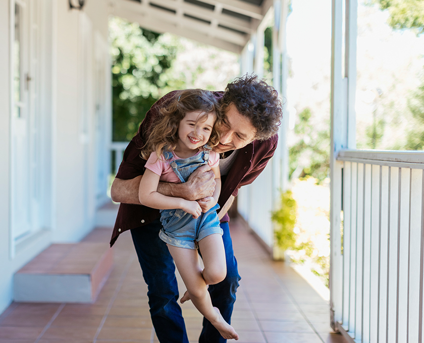 uncle lifting up his young laughing barefoot niece on large front porch on a sunny day