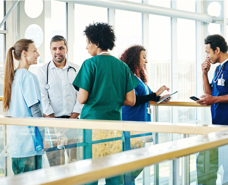 Group of medical staff of various ages talking in hospital corridor during work break