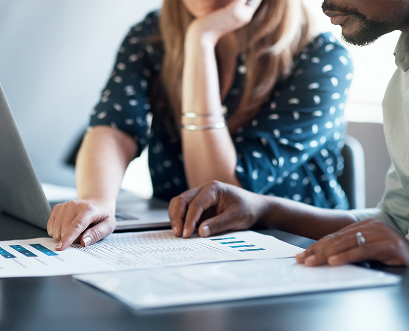 coworkers reviewing papers with laptop open and woman pointing to graphic on page