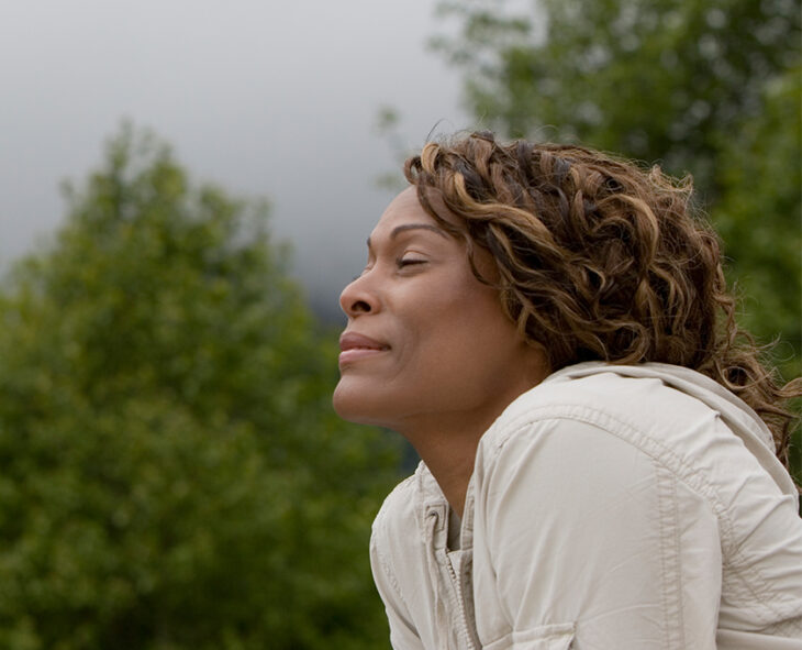 Profile of mature woman with closed eyes taking a deep breath and smiling with trees in background