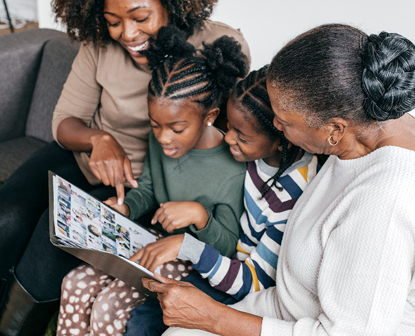 grandmother and mother with two girls sitting between them smiling and pointing at photo album they are flipping through