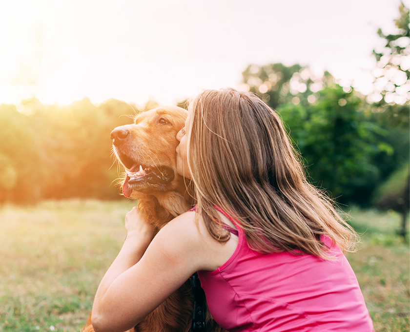 woman in park crouched next to golden retriever kissing the dog's cheek