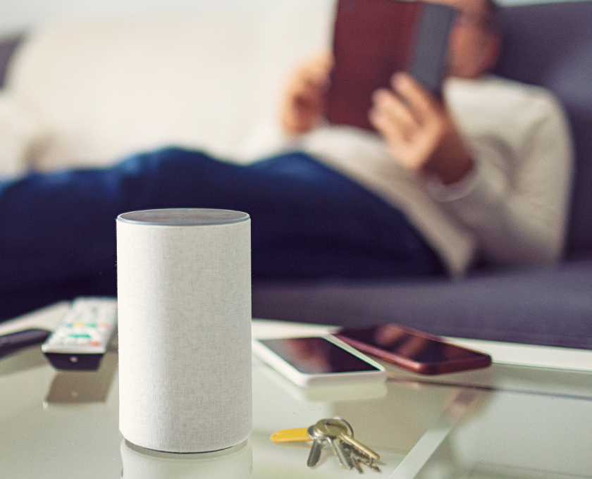 man laying on couch looking at tablet with mobile phone and smart speaker on table