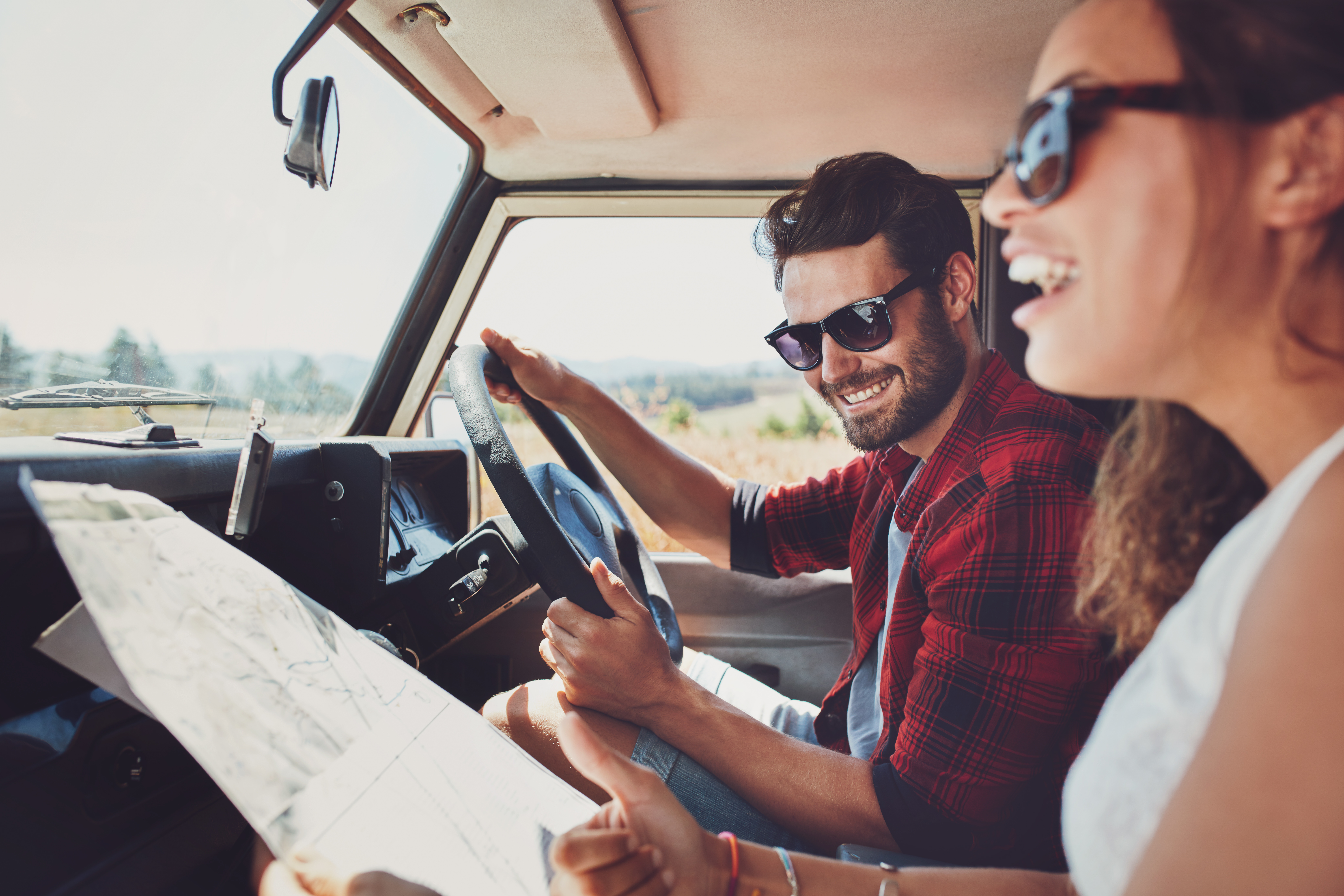 Couple happily driving in a car, with the woman holding a map and the man smiling at the wheel