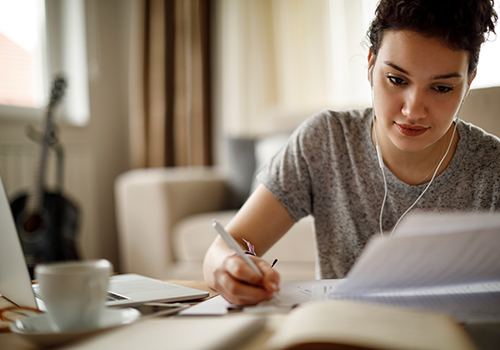 Young woman writing at home with a laptop and cup of coffee and notebooks on the table