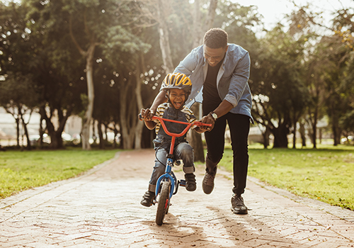 Ecstatic little boy learning to ride a bicycle with his father