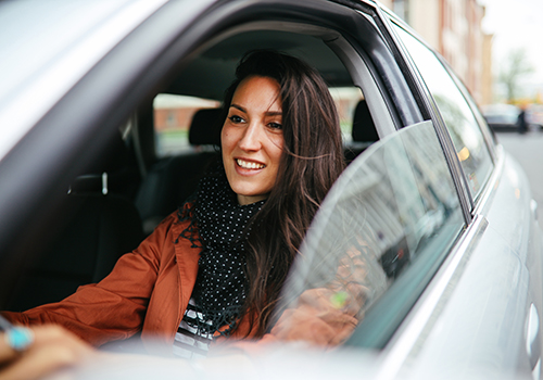 Young woman driving through downtown with window open.