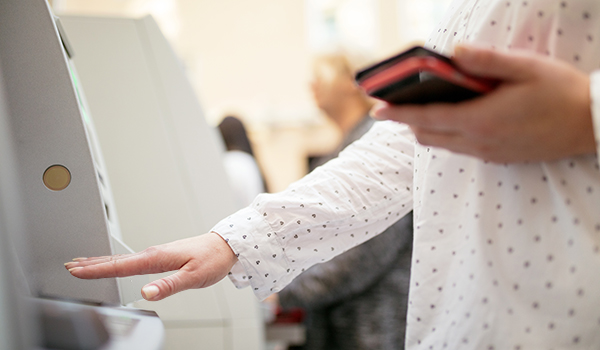 close up of woman standing at ATM holding wallet in one hand and scanning other palm