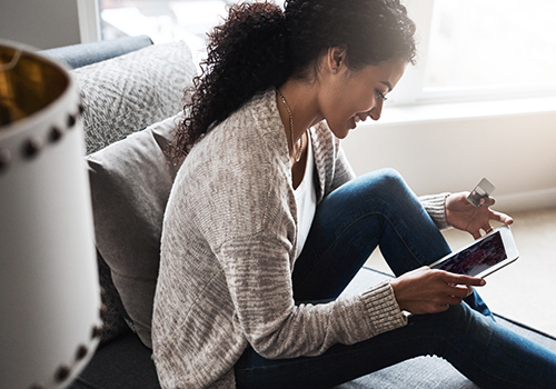 Cheerful young woman using her Allegacy Credit Card to do online shopping with a digital tablet at home
