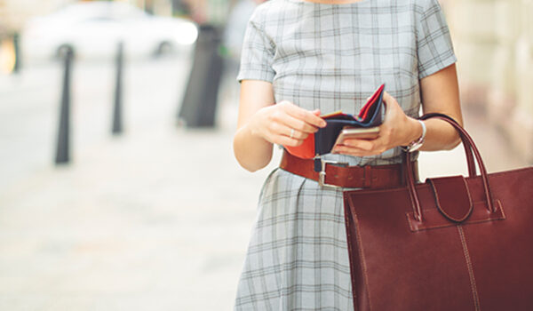 woman in dress on sidewalk looking in a red wallet