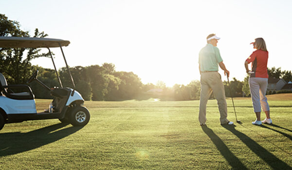 golfers, one man and one woman, standing on the green near a cart