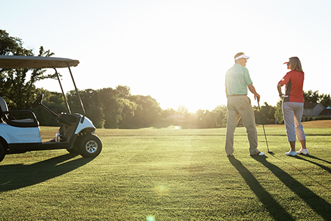 golfers, one man and one woman, standing on the green near a cart