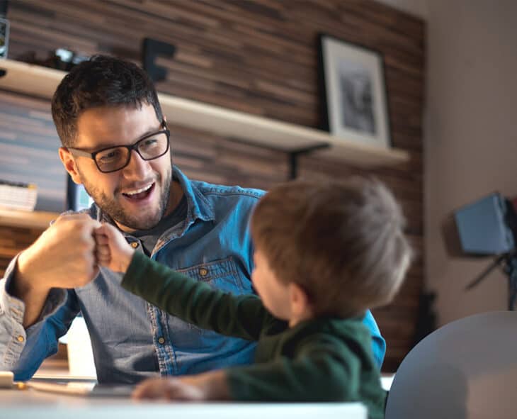 Dad and son fist bumping in front of computer at home.