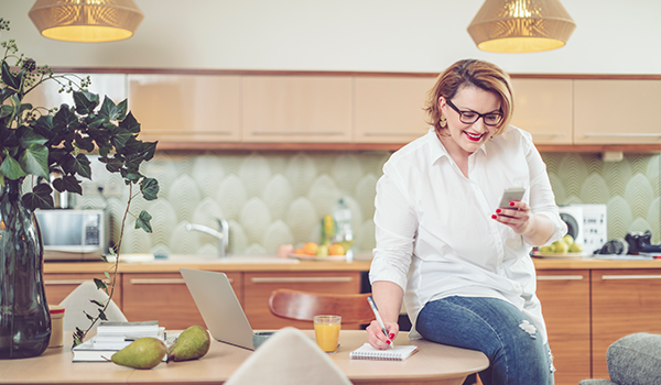 Lady sitting on desk with laptop taking notes on a notepad