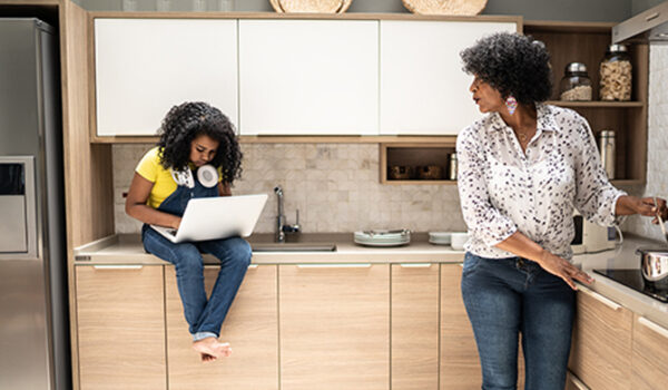 Girl using laptop sitting on kitchen counter while grandmother is cooking