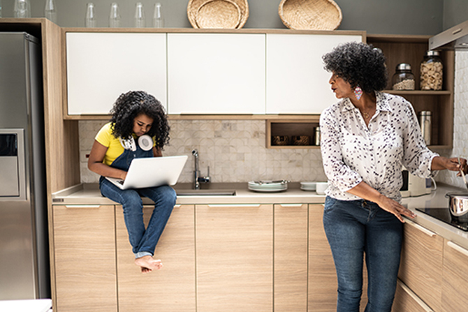 Girl using laptop sitting on kitchen counter while grandmother is cooking