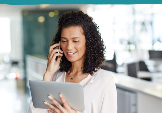 woman talking on phone and viewing tablet in office space setting