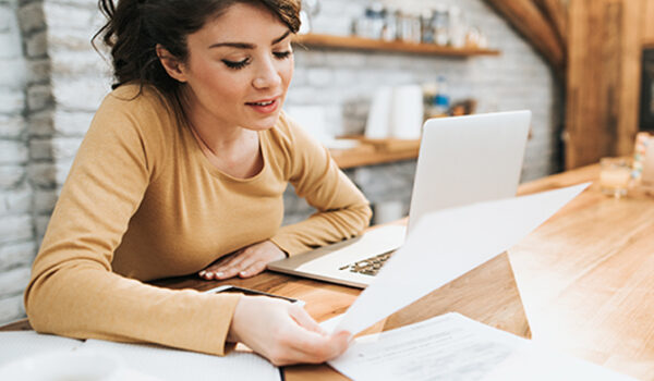 woman at kitchen counter looking at laptop and papers