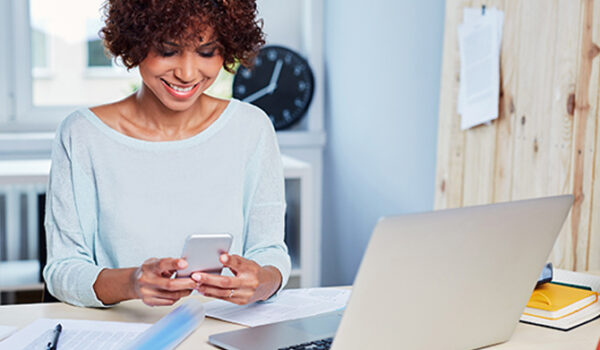 Woman looking at phone with laptop on desk