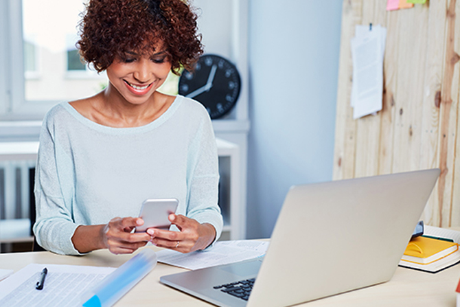 Woman looking at phone with laptop on desk