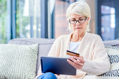 Senior woman using a digital tablet and credit card on the sofa at home