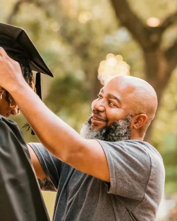 man adjusting graduation cap on student graduate